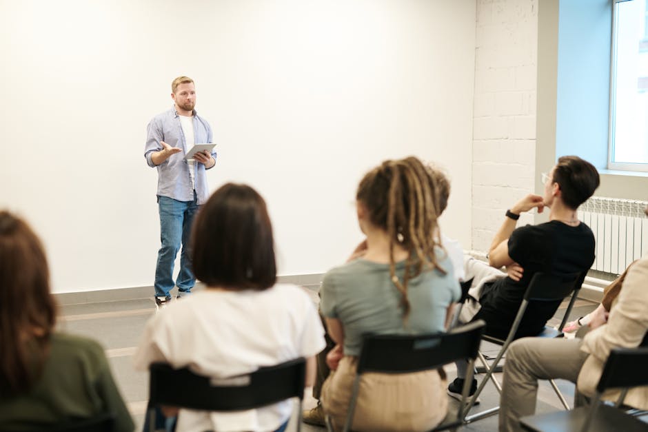 Man presenting with tablet to a small seated audience in a modern indoor setting